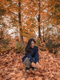 Portrait of young woman sitting on tree during autumn