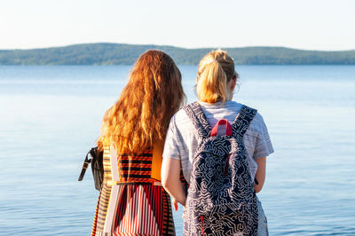 Rear view of women at sea shore against sky