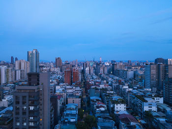 Aerial view of buildings in city against blue sky