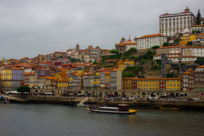 Boats in river by buildings in city against sky