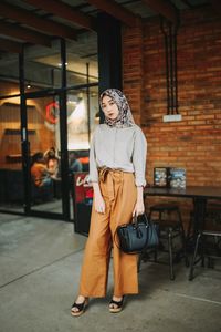 Portrait of young woman standing against brick wall