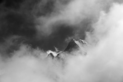 Low angle view of foggy high altitude mountain against sky