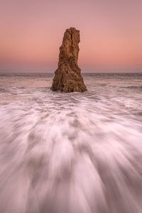 Rock in sea against sky during sunset