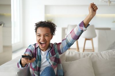 Portrait of young man with arms raised sitting on bed at home