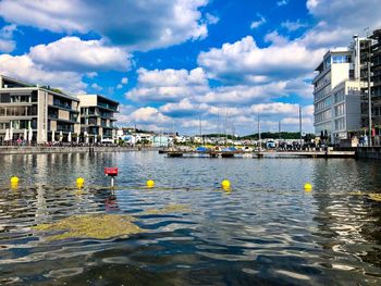 Boats in river by buildings in city against sky