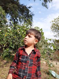 Boy looking away while standing against trees