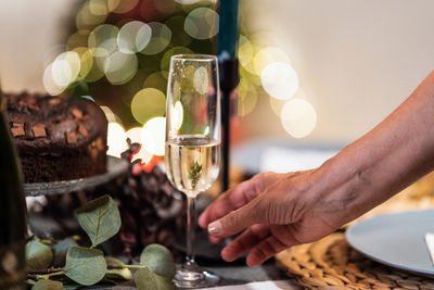 Unrecognizable female in glittering dress standing in room with glass of champagne during christmas party