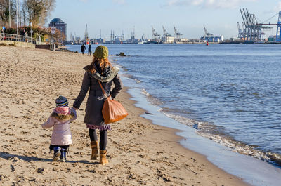 Rear view of mother and daughter walking on beach