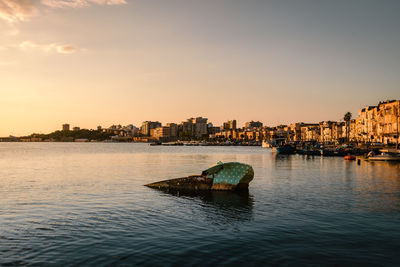 Scenic view of river by buildings against sky during sunset