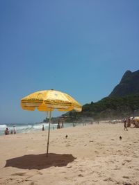 A beautiful sunny day, a yellow umbrella on the beach, people and pigeons. 