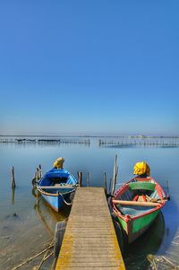 Boats moored at pier against clear blue sky