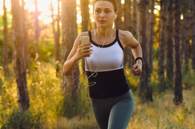 Midsection of woman running on mobile phone in forest