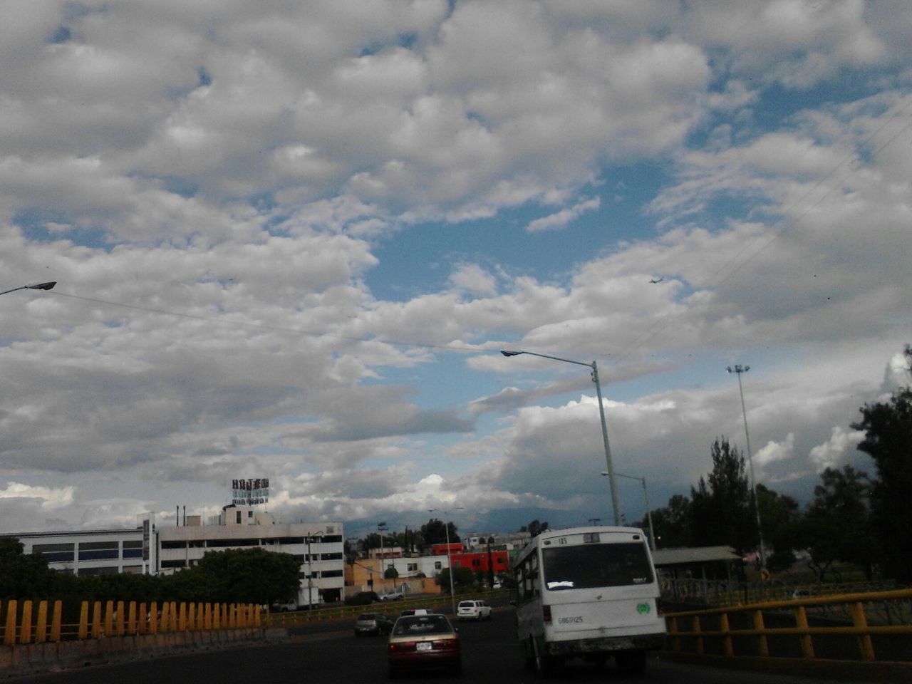 sky, transportation, cloud - sky, car, land vehicle, cloudy, mode of transport, building exterior, road, built structure, architecture, street, cloud, overcast, city, weather, outdoors, street light, on the move, day