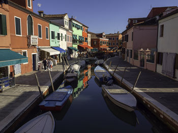 Boats moored in canal by buildings against sky