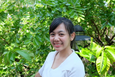 Portrait of smiling young woman standing against trees