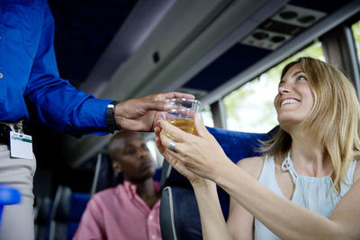 Guide giving drink to happy woman in bus