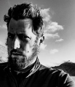 Close-up portrait of serious mid adult man against sky during sunny day