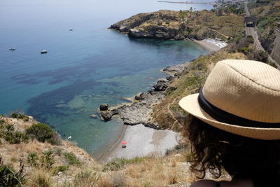 Woman wearing straw hat on cliff by sea at capo zafferano