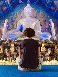 Rear view of woman sitting against buddha statue at temple