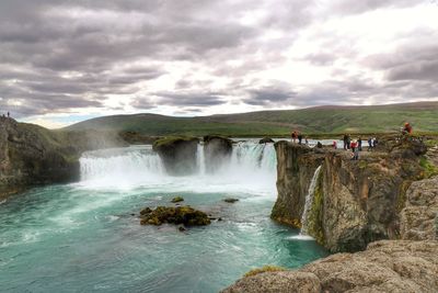 Scenic view of waterfall against cloudy sky