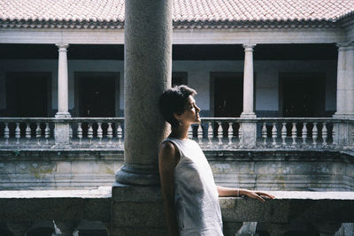 Side view of woman sitting by window against building