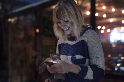 Happy woman using smart phone in illuminated city at night