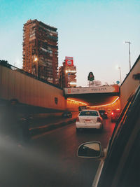 Cars on street by illuminated buildings in city against sky