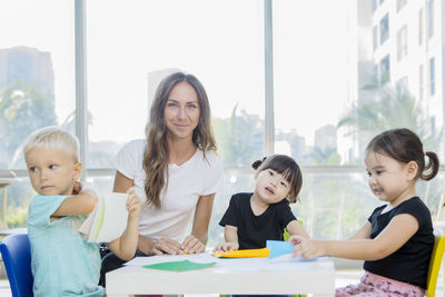 Portrait of mid adult teacher sitting with students in classroom at school