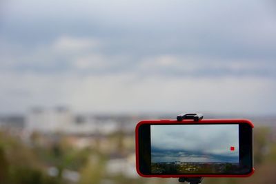 Close-up of mobile phone on monopod against cloudy sky