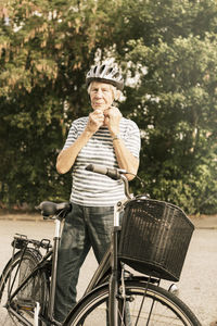 Senior woman wearing helmet while standing by bicycle on road