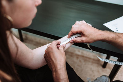 High angle of unrecognizable male master measuring part of arm of female customer for applying tattoo