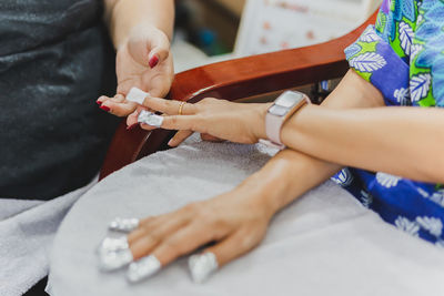 Woman in nail salon receiving a manicure by a beautician with cotton wool