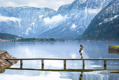 Side view of young woman walking on footbridge over lake during winter