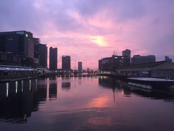 Buildings by river against sky during sunset