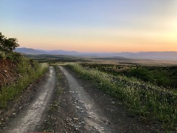 Empty road amidst field against sky during sunset