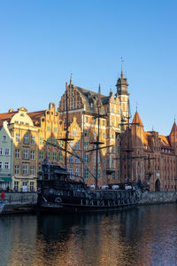 View of buildings by river against clear sky