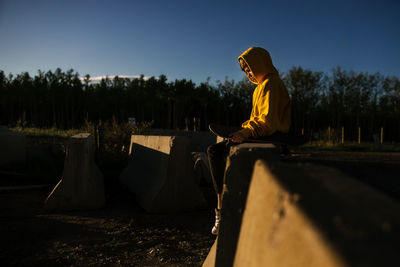 Teen boy with skateboard sitting on concrete