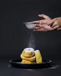 Hand adding powdered sugar on donuts against black background