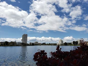 View of buildings by river against cloudy sky