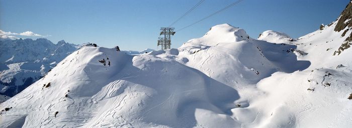 Tower of cable car on snow covered mountain against sky