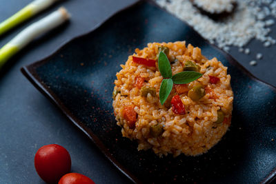 Italian vegan spring risotto on black dish with asparagus on dark dish with colorful pepper parsley