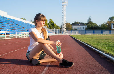 Sports and fitness. teenager girl sitting on stadium track having rest drinking water