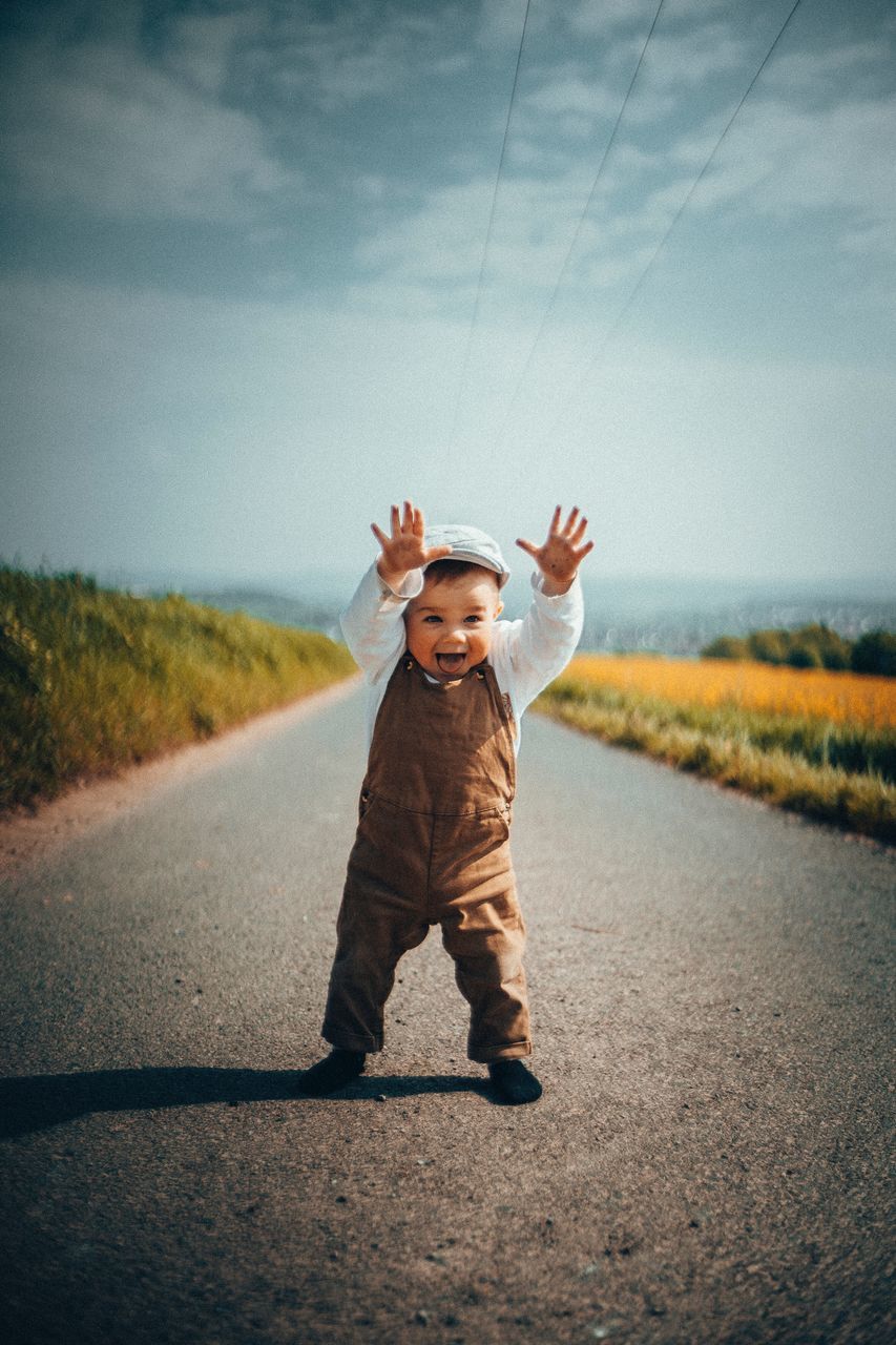 childhood, road, child, full length, one person, sky, transportation, human arm, nature, day, real people, men, leisure activity, casual clothing, field, front view, arms raised, standing, outdoors, innocence, positive emotion