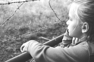 Close-up of thoughtful girl by barbed wire fence