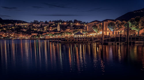 Illuminated buildings by lake against sky at the beginning of the night and the end of the blue hour