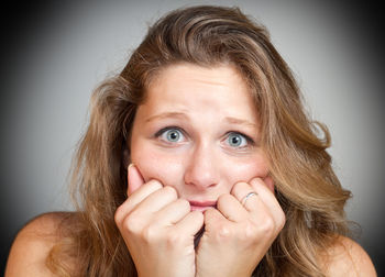 Close-up portrait of scared young woman with head in hands against gray background