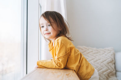 Cute little toddler girl in yellow longsleeve looking in window at the home