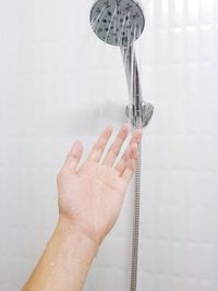 Cropped hand of woman under shower in bathroom