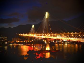 Illuminated bridge over river against sky at night