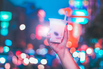 Cropped hand holding drink against illuminated background
